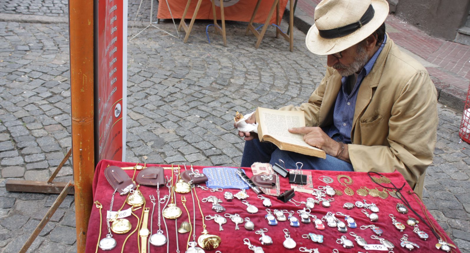 A streetside vendor reads as shoppers jostle past at the San Telmo Sunday Market